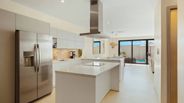 Una cocina moderna con una isla central, electrodomésticos de acero inoxidable y vistas a una zona de piscina.