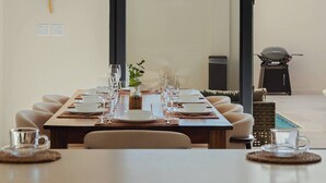 Un comedor con una larga mesa dispuesta para una comida, una parrilla al fondo y vista al cielo.