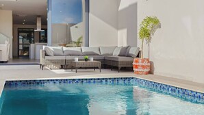 Un área de piscina moderna al aire libre con un espacio para sentarse y una planta en maceta.