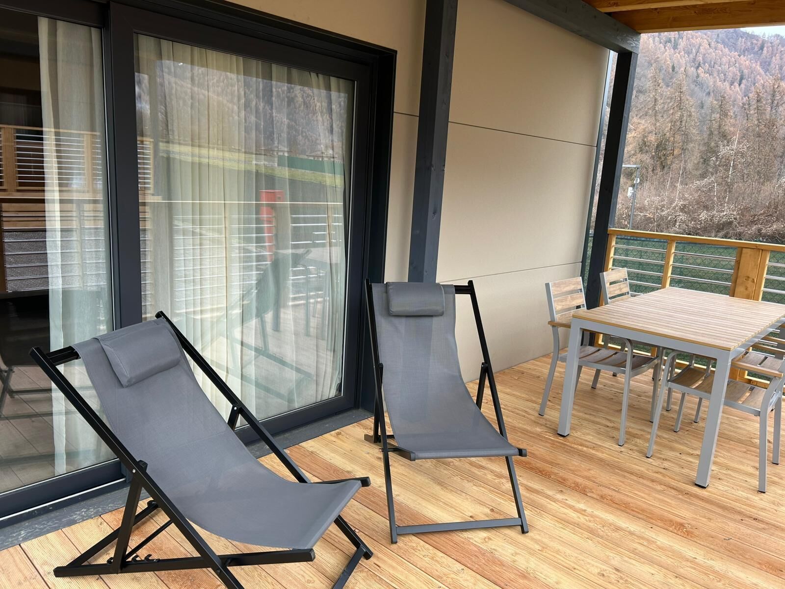 Een balkon met twee ligstoelen en een tafel, met uitzicht op een bebost gebied.