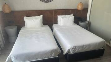 Habitación de hotel con dos camas individuales, un adorno redondo en la pared y dos lámparas colgantes.