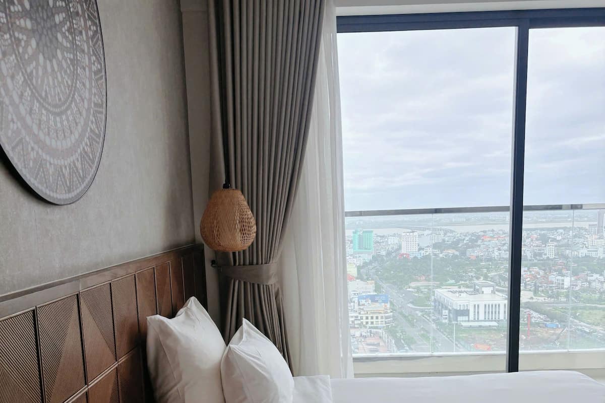 Een hotelkamer met twee bedden, een groot raam met uitzicht op de stad, een decoratieve wandbekleding met een patroon en een lamp met een structuur.