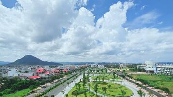A cityscape with a prominent mountain in the background, a wide road with greenery, and modern buildings.