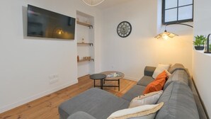 A modern living room with a grey sofa, a small round table, and a wall-mounted TV. - Cœur de Pau - Clim et Parking - L'Odyssée (Pau)