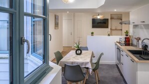 A modern kitchen with a dining area, a TV mounted above the counter, and a window with a view of the outside. - Cœur de Pau - Clim et Parking - L'Odyssée (Pau)