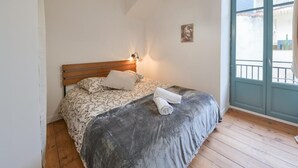 A bedroom with a wooden bed, a grey blanket, and a white pillow. - Cœur de Pau - Clim et Parking - L'Odyssée (Pau)