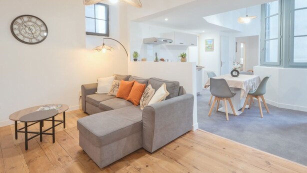 A modern living room with a grey sectional sofa, a small table, and a dining area with a white table and chairs. - Cœur de Pau - Clim et Parking - L'Odyssée (Pau)