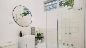 A bathroom with a toilet, sink, mirror, and shower. - Cozy House Ideal Location (Melbourne)