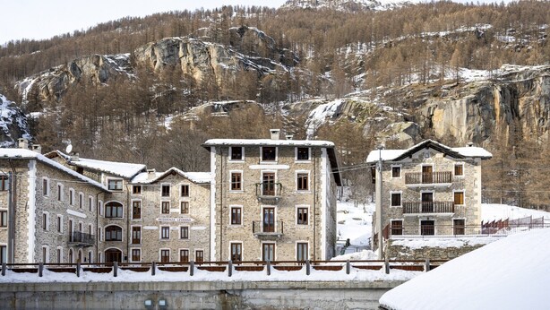Un edifici de pedra amb nombroses finestres i balcons, envoltat d'un paisatge nevat i muntanyes.