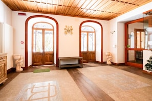 A hotel lobby with wooden flooring, two large arched windows, a bench, and a small table.