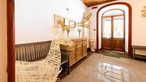 Zona de recepció amb un banc de fusta, una cadira trenada, un armari de fusta i una porta amb panells de vidre.