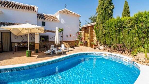 A swimming pool with a tiled edge, surrounded by a patio area with lounge chairs and umbrellas. - Holiday Home in Archidona with private pool (Archidona)