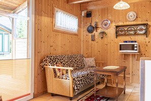 Een gezellige kamer met een sofa met luipaardprint, een houten eettafel, een magnetron en een raam met blinds.