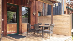 Una terraza de madera con una mesa y sillas, una puerta verde y una valla de madera.