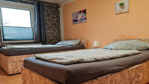 Quarto com duas camas, janela com persianas, parede de pedra e um quadro com flores.