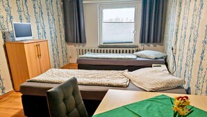 A small, tidy room with a bed, a desk, a chair, a radiator, and a window with curtains. - Cosy apartment in the Oderbruch (Bleyen-Genschmar)