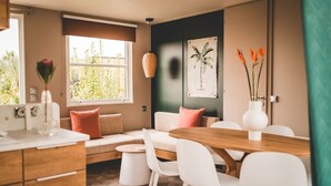 Un salon moderne avec un canapé, une table à manger et des chaises. Une fenêtre offre une vue sur la verdure à l’extérieur.