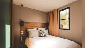 Une chambre à coucher avec une tête de lit en bois, un lit avec une literie blanche, un luminaire suspendu et une fenêtre avec des rideaux.