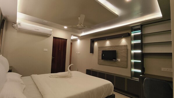 Una habitación de hotel moderna con cama, televisor de pantalla plana montado en la pared, ventilador de techo y estanterías empotradas.