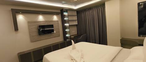 Une chambre d’hôtel moderne dotée d’un téléviseur à écran plat fixé au mur, d’un lit avec une serviette soigneusement pliée, d’un bureau avec une chaise et d’une grande fenêtre avec des rideaux.