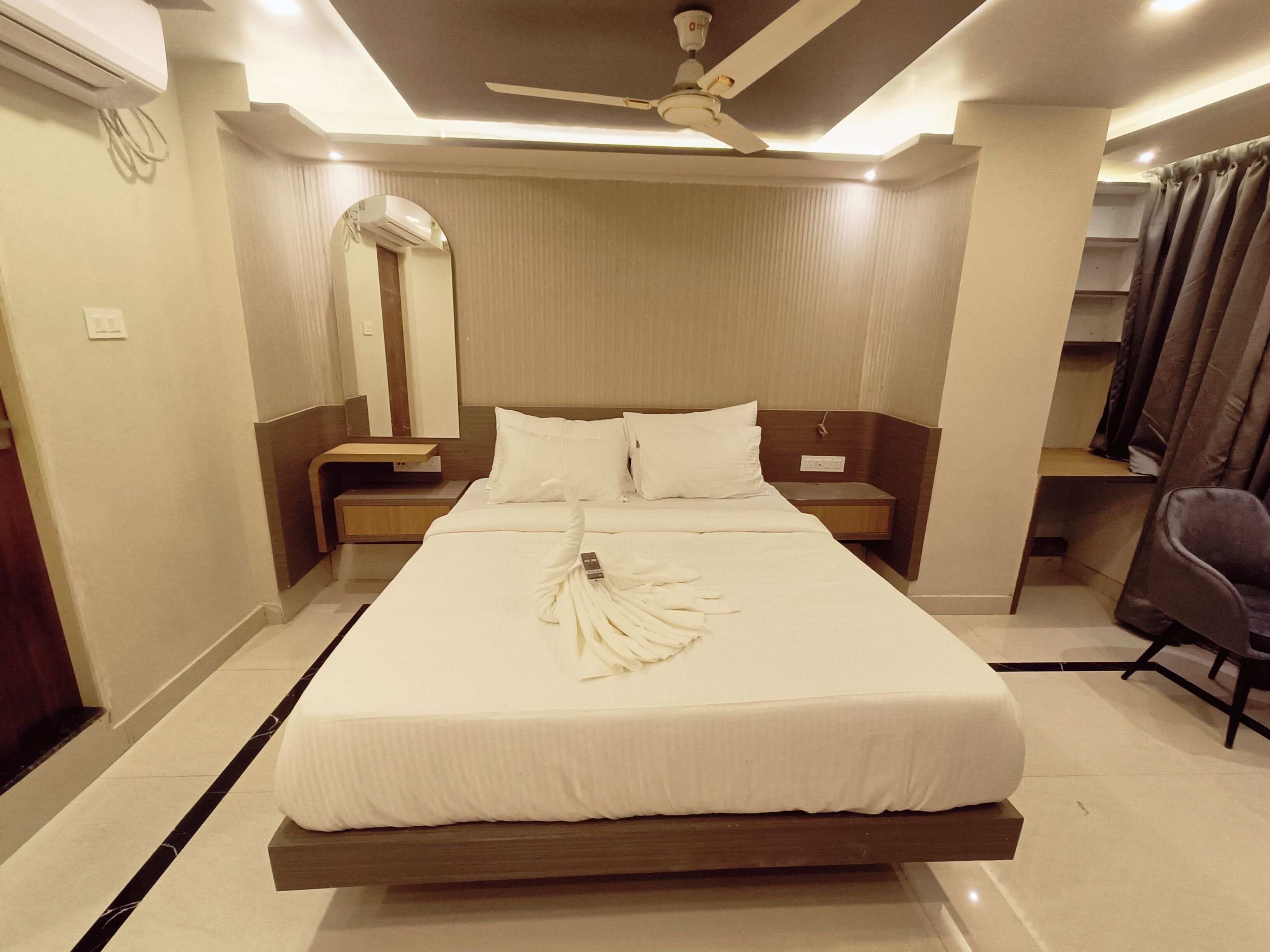 Une chambre d’hôtel comprenant un lit, une table de chevet, un miroir, un ventilateur de plafond et une chaise.