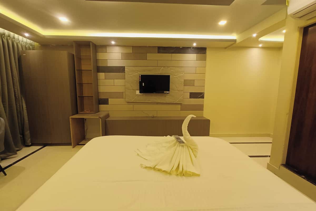 A hotel room with a neatly made bed, a flat-screen TV mounted on a wall with a stone-like pattern, a bedside table, and a curtain on the left.