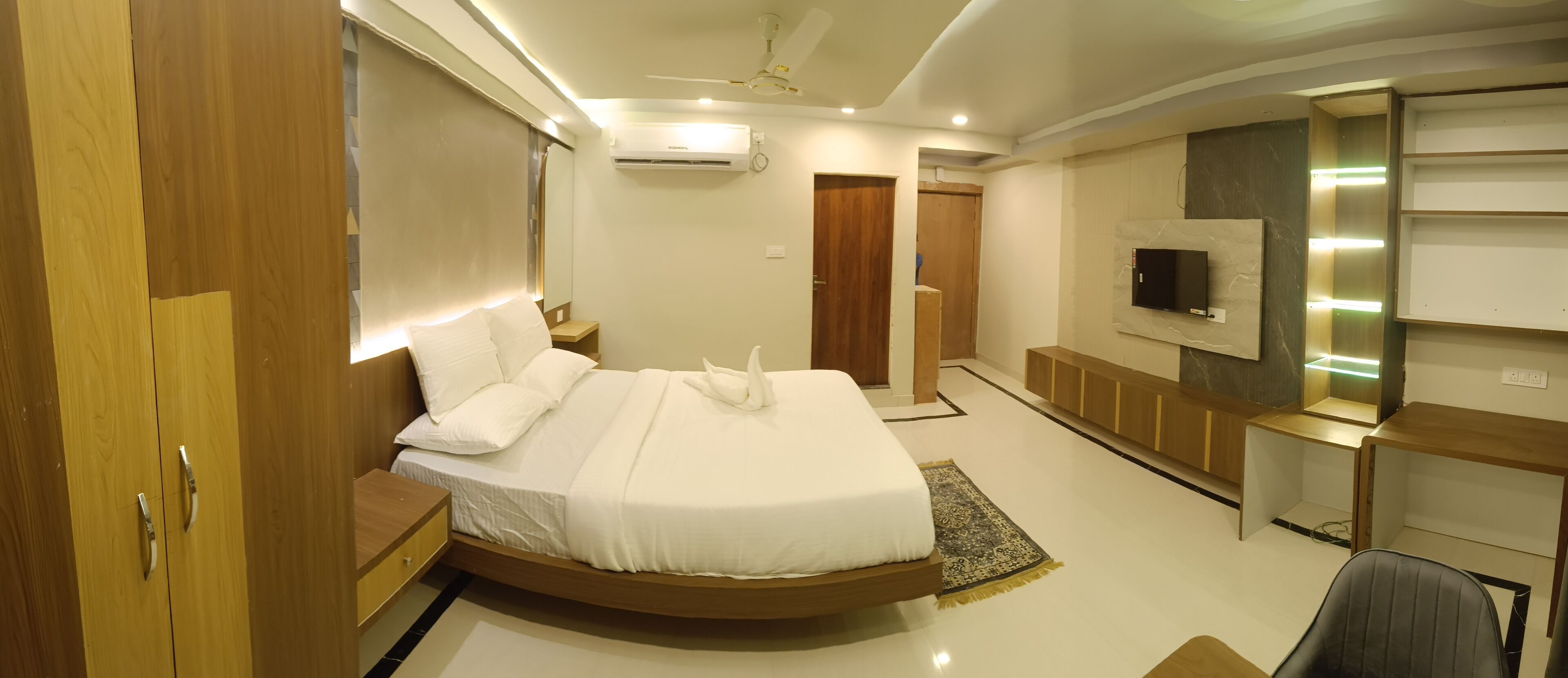 A modern bedroom with a curved bed, a TV mounted on the wall, and a ceiling fan.