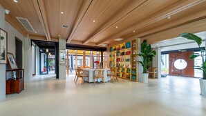 A spacious lobby with a wooden ceiling, a central seating area with tables and chairs, and a large bookshelf filled with colorful items. - Silk Road-Fu Tea Town Boutique Homestay (Xianyang)