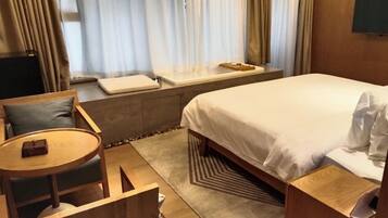 Habitación de hotel con cama, una pequeña mesa redonda con silla, sofá y ventana con cortinas.