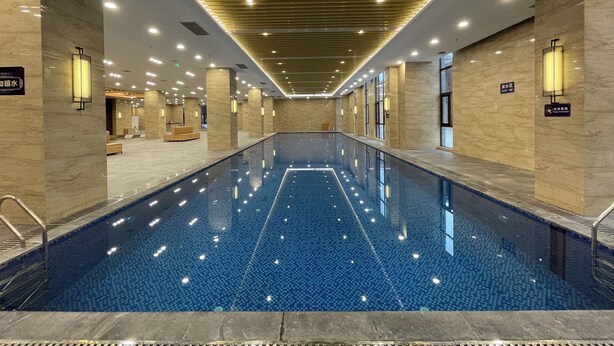 A large indoor swimming pool with a tiled floor, surrounded by marble walls and equipped with overhead lighting. - Silk Road-Fu Tea Town Boutique Homestay (Xianyang)