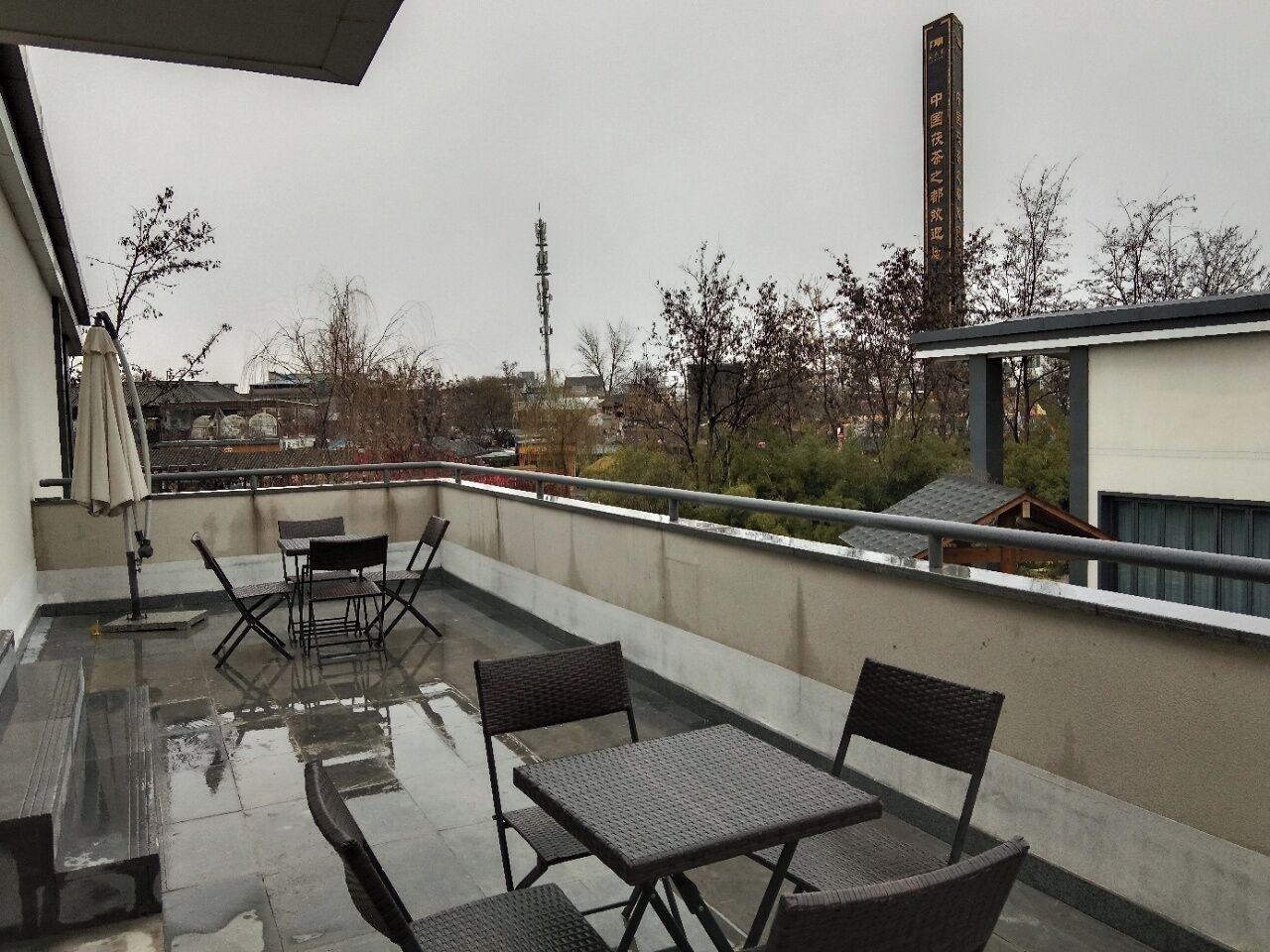 Een dakterras met een tafel en stoelen, een hekwerk en uitzicht op gebouwen en bomen.
