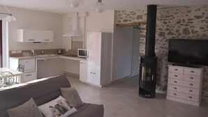 Ett modernt kök med vita skåp, en mikrovågsugn och en spis. Det finns en soffa med kuddar och en tv som står på ett TV-bord.