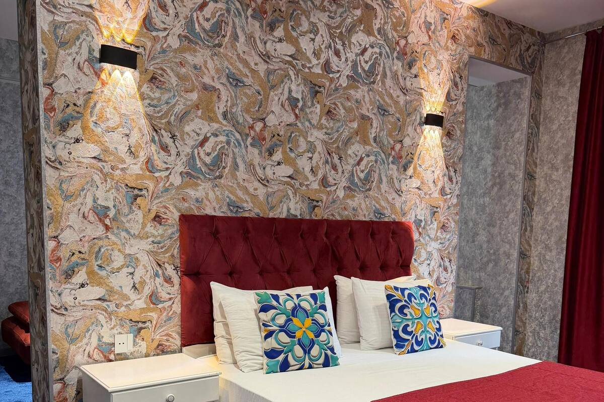 Camera da letto con parete effetto marmo, testiera imbottita rossa e comodino bianco con cassetto.