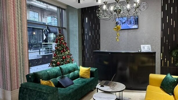 A modern living room with a green sofa, a yellow sofa, a coffee table, a TV mounted on the wall, and a Christmas tree. - Avenue Nizami Hotel (Baku)
