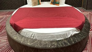 A circular bed with a red blanket, two pillows with multicolored patterns, and a dark headboard with two wall-mounted lights. - Avenue Nizami Hotel (Baku)