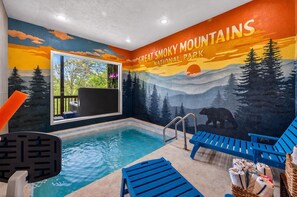Ein Swimmingpool mit Wandgemälde der Great Smoky Mountains, ein Fenster mit Aussicht und blaue Liegestühle.