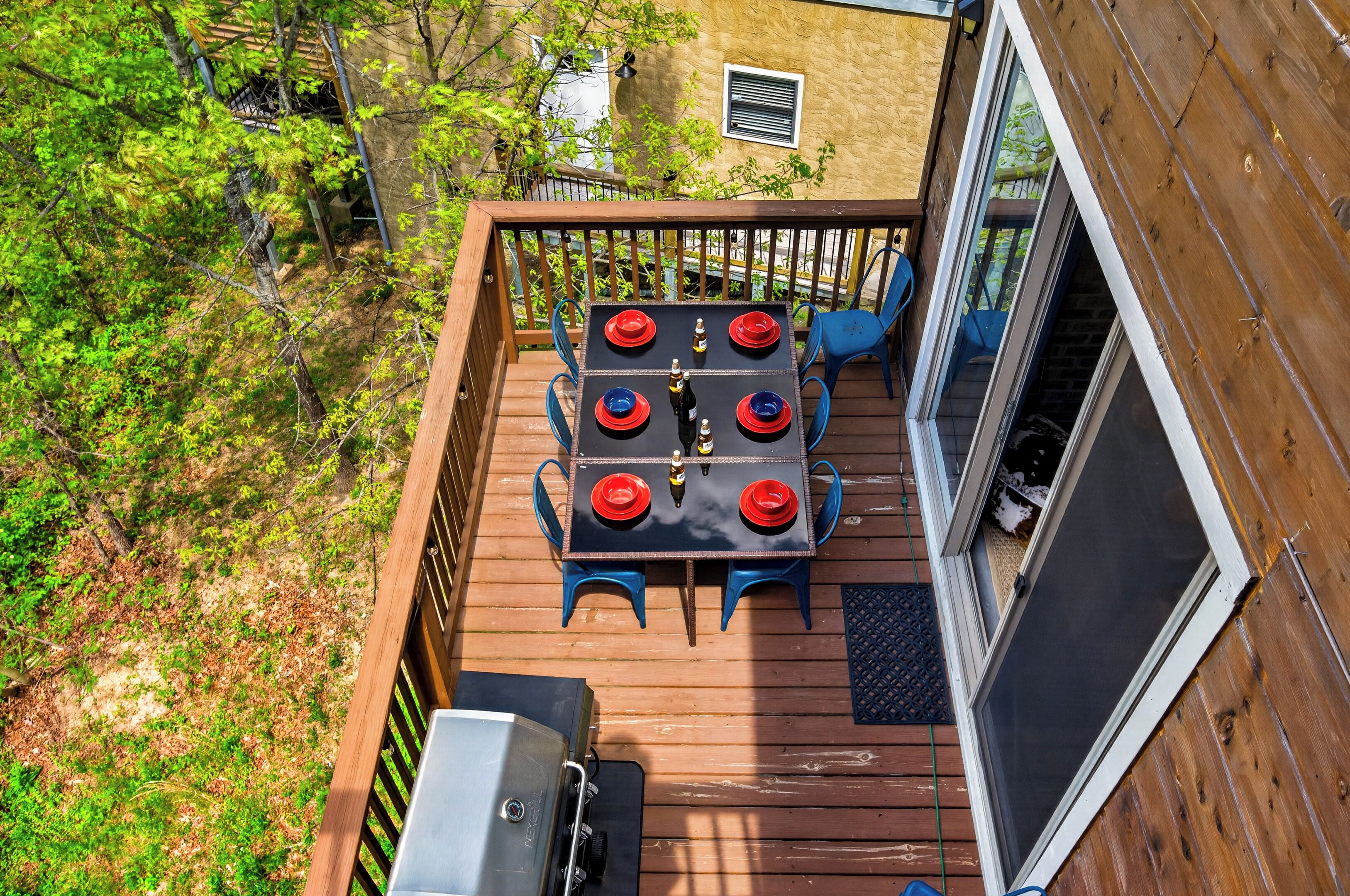 A wooden deck with a table set for four, a grill, and a view of a forested area.