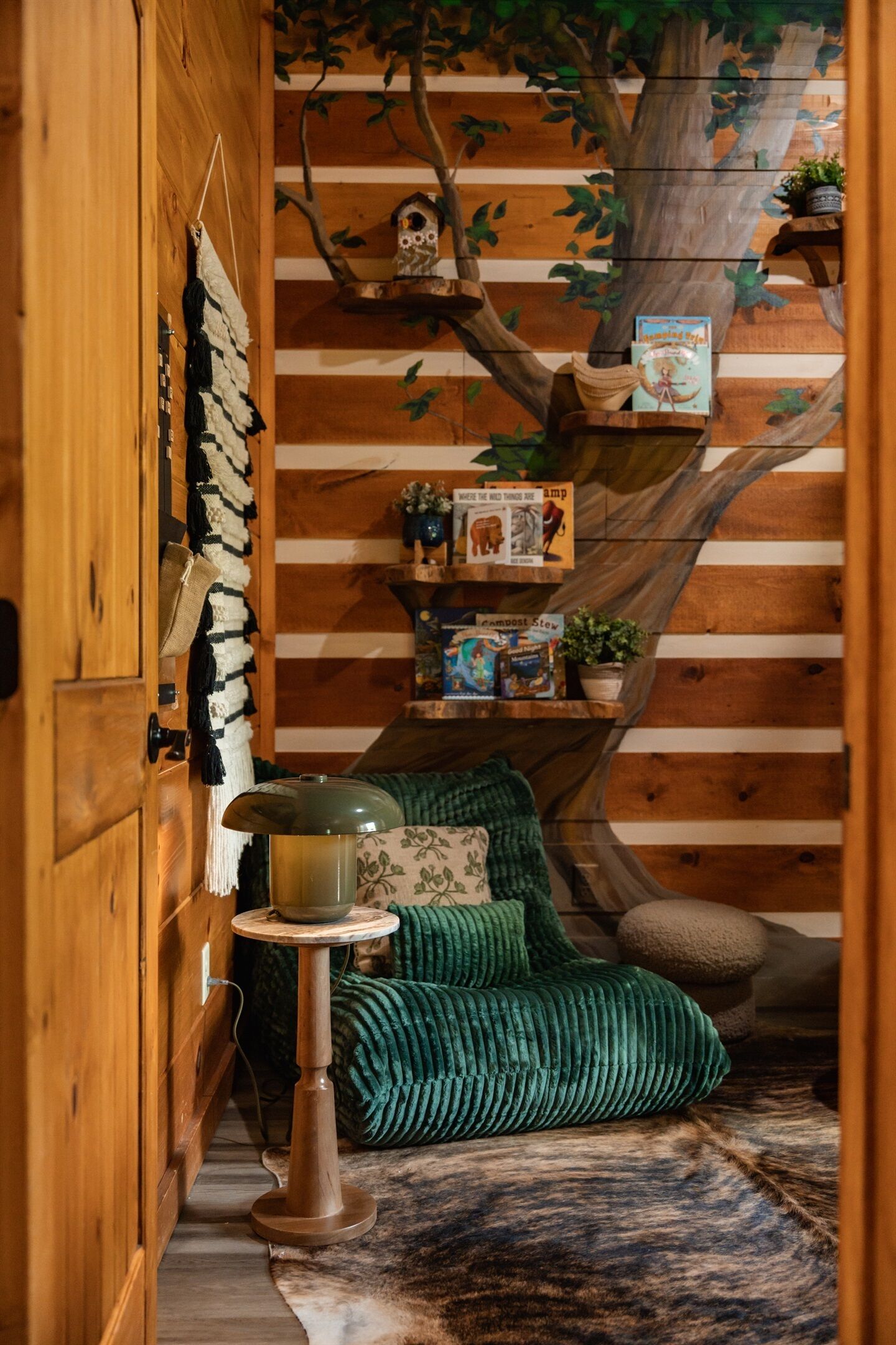 Ein gemütlicher Raum mit Holzwand, einem grünen Sofa, einem kleinen Tischchen mit einem Topf und einem Baum-Wandbild.