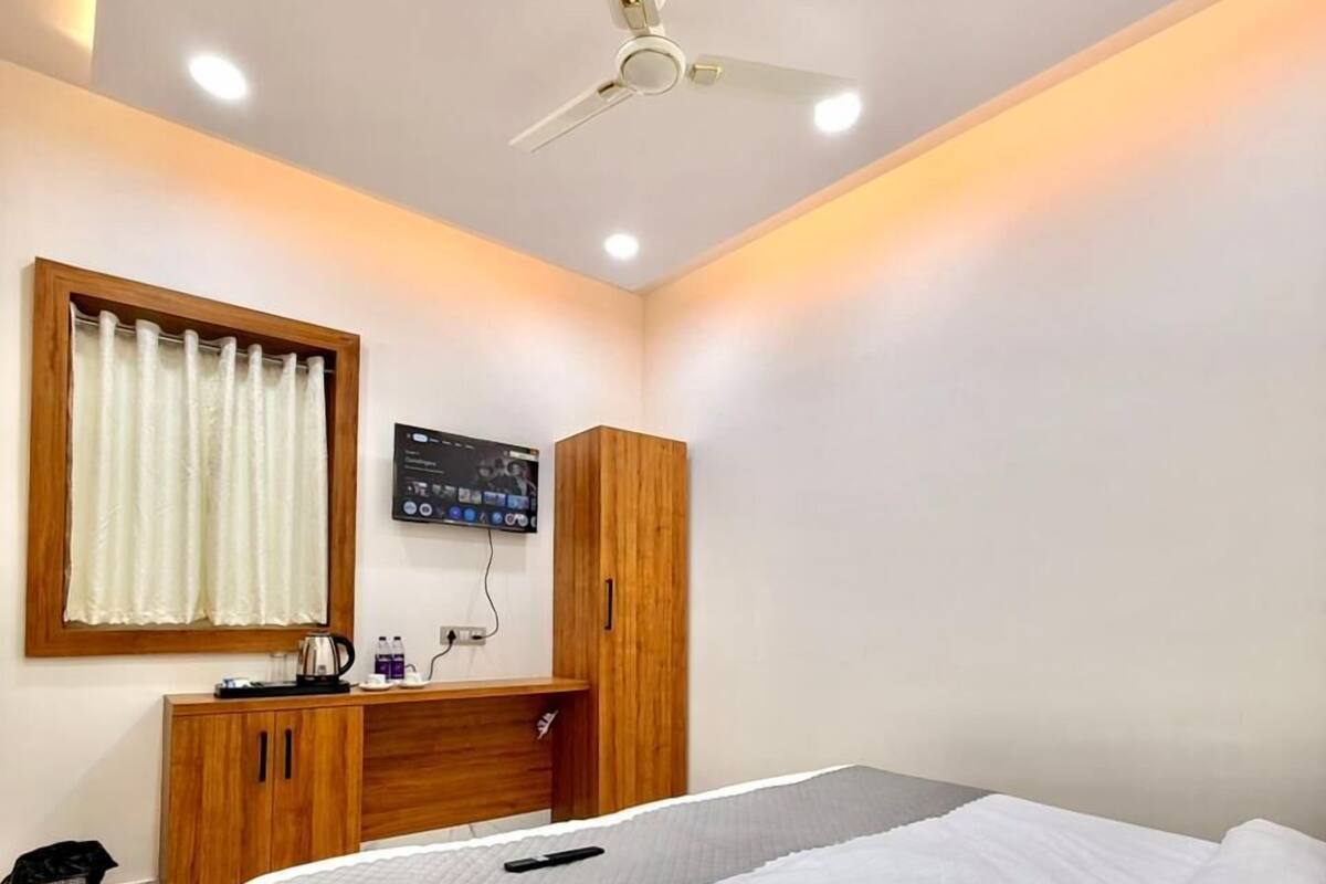Un dormitorio con cama, armario de madera, ventilador de techo, televisor y una pequeña mesa con tetera.