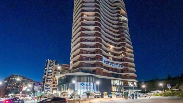 A modern hotel with a curved facade, multiple balconies, and a prominent entrance with glass doors. - HB apartments University Agro (Tbilisi)