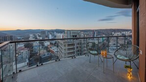 A balcony with a city view, two wicker chairs, a small table, and a vase with lights. - HB apartments University Agro (Tbilisi)