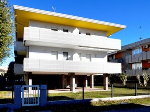 A modern building with a flat roof, two levels, and a yellow accent on the upper level. - Central cozy house - Beahost (Bibione)