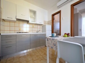 A compact kitchen with grey cabinets, a tiled backsplash, and a small dining table with a blue tablecloth. - Central cozy house - Beahost (Bibione)