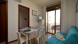Una stanza piccola e luminosa con un tavolo da pranzo, sedie, un divano e un balcone con vista.