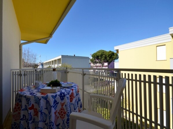 An outdoor balcony with a table covered in a fish-patterned tablecloth, a white chair, and a yellow umbrella. - Central cozy house - Beahost (Bibione)