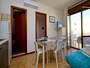 A small, well-lit room with a dining table, chairs, a bed, and a balcony with a view. - Central cozy house - Beahost (Bibione)