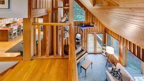 Ein geräumiges Loft mit Klavier, einer Couch und einem großen Fenster mit Blick auf einen Wald.