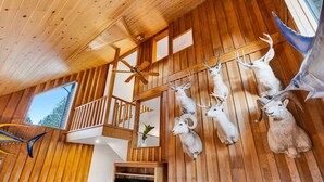 Ein Holzinnenraum mit an der Wand befestigten Tierköpfen, einem Deckenventilator und einer Treppe.