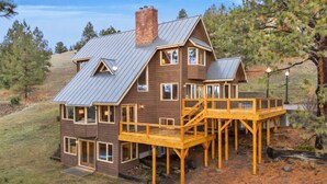 Ein zweistöckiges Holzhaus mit Metall-Dach, einer Holzterrasse und einem Schornstein.