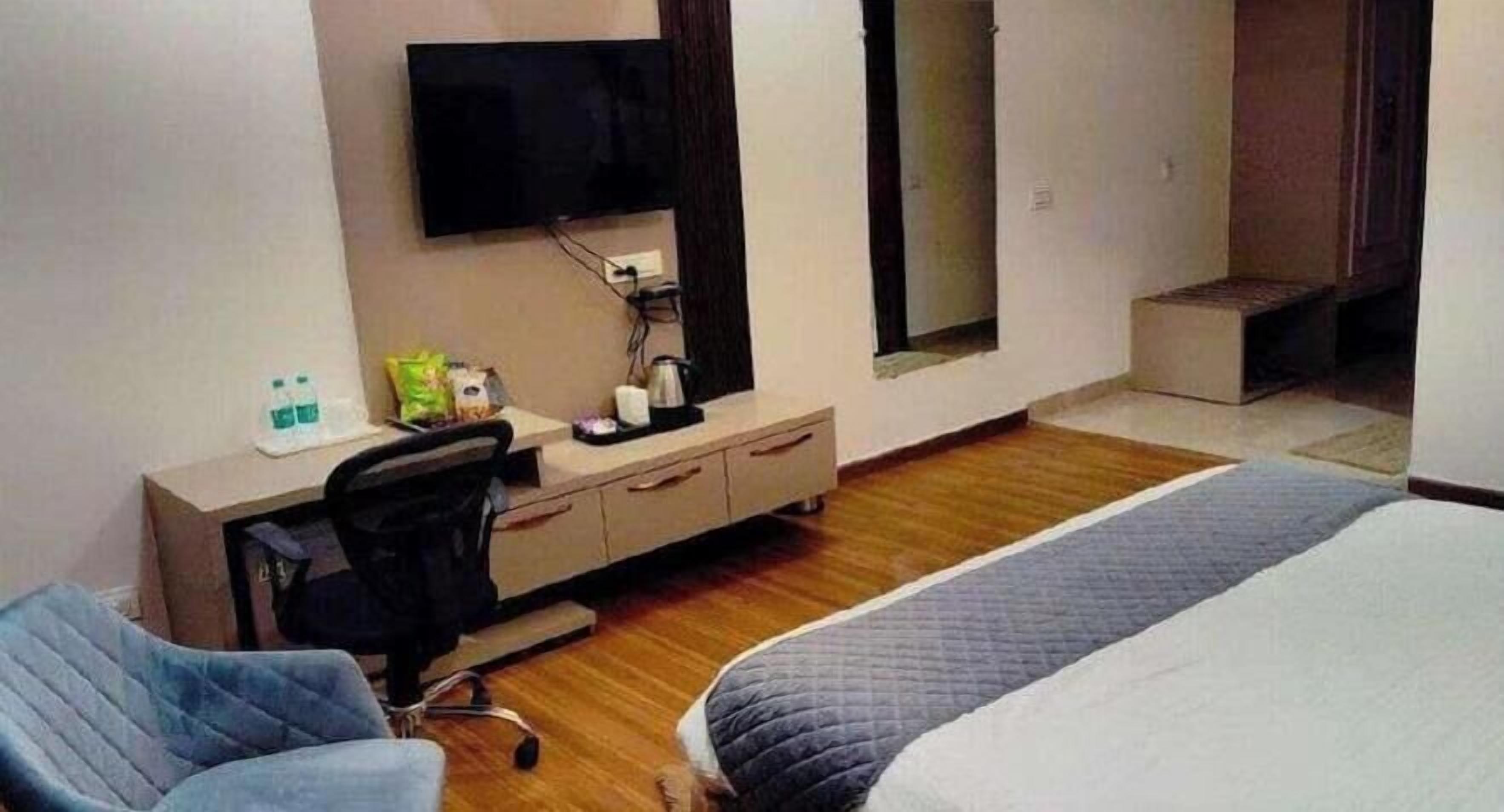 Una habitación de hotel con cama, escritorio, silla, televisor y ventana.